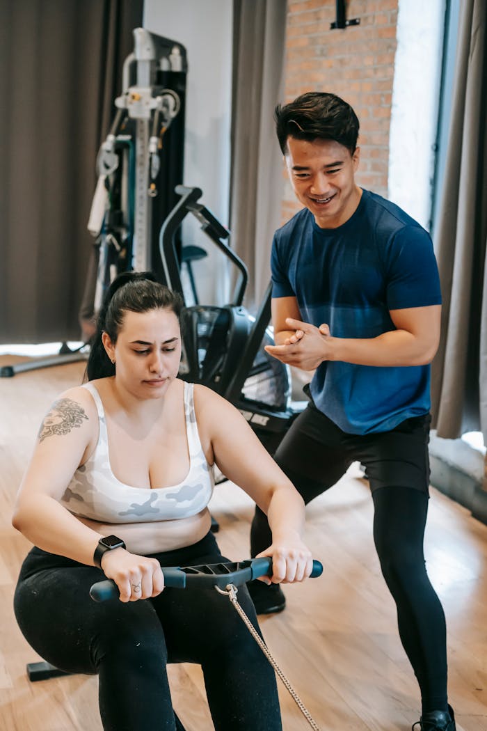 why-choose-us From above of positive ethnic trainer smiling and helping plus size female doing exercise on rowing machine in gym